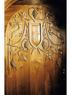 Hand-carved solid wood wine cellar door featuring deep-relief vineyard crest, grape vines, and rich natural wood tones