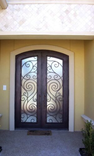 Arched wrought iron door EL1113 MCD with flowing scrollwork and frosted glass, hand-forged for elegance and privacy.