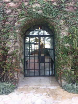 Rustic arched wrought iron door EL1166 MCD with grid glass panels, hand-forged for elegance and durability.