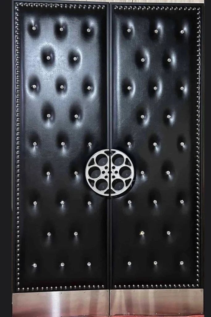Black tufted double home theater door HT3019 MCD featuring a silver film reel centerpiece, studded trim, and metal kick plates