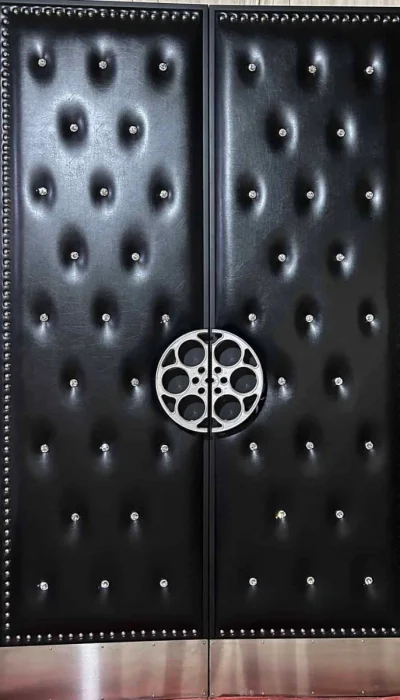 Black tufted double home theater door HT3019 MCD featuring a silver film reel centerpiece, studded trim, and metal kick plates